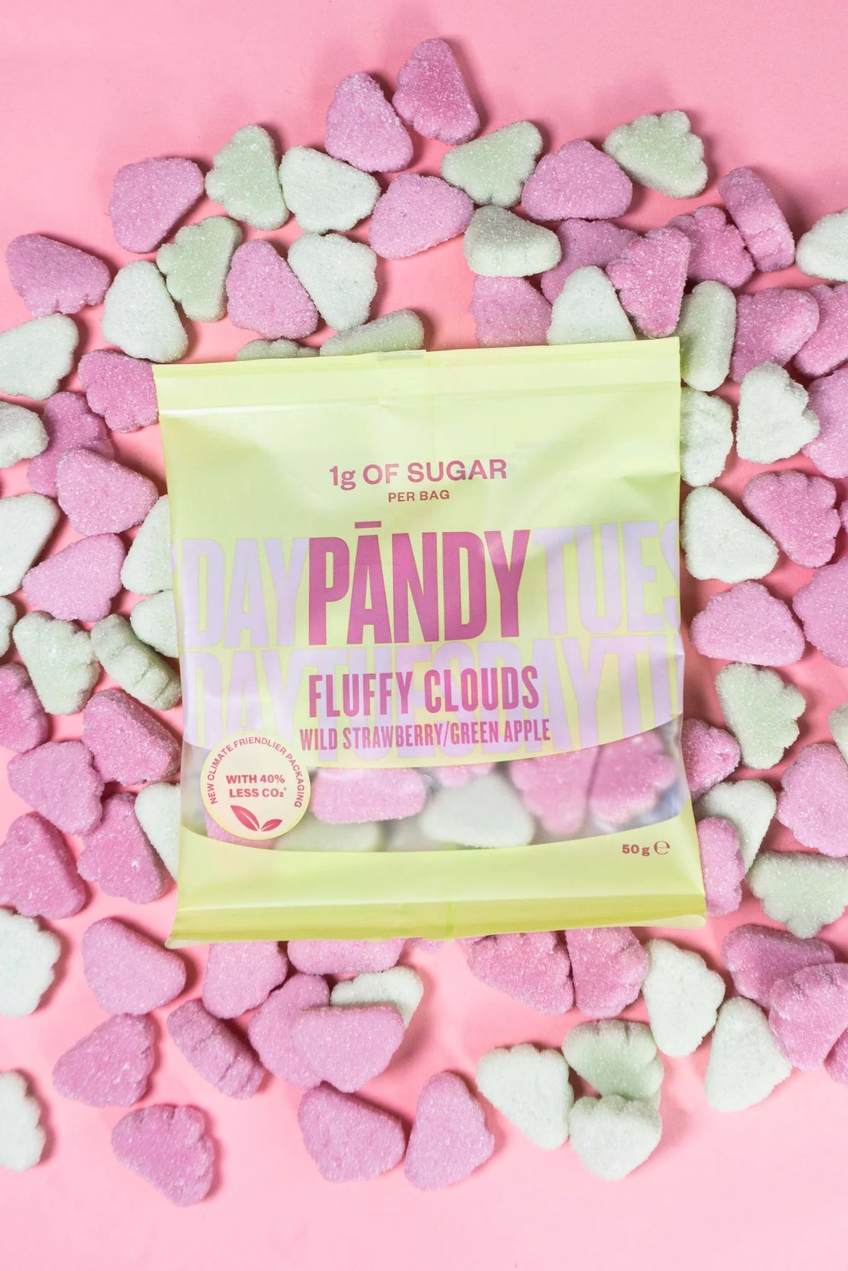 A bag of Pândy Fluffy Clouds candy in Wild Strawberry and Green Apple flavor, surrounded by pink and mint green heart-shaped sugar-coated candies on a solid pink background.